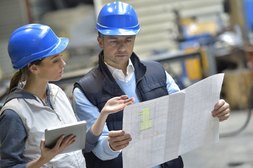Engineers in hard hats reading blueprints in factor