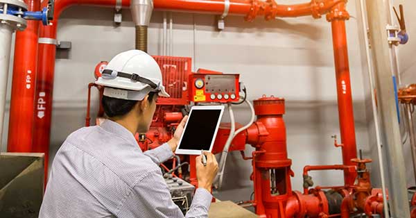 Man inspecting fire safety equipment using digital forms on tablet.
